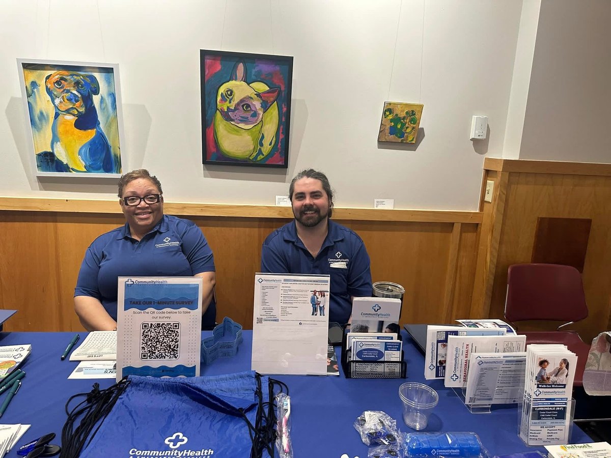 Two men sitting at a blue table with merchandise and a QR code display at a community outreach booth